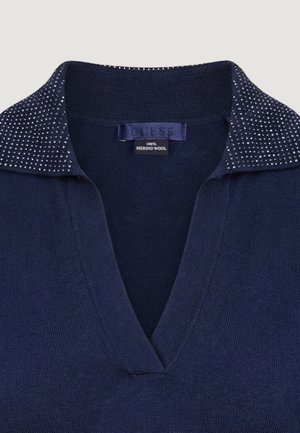 Pull col en V en laine mérinos bleu marine avec col orné et étiquette de la marque Guess visible à l'intérieur du col.