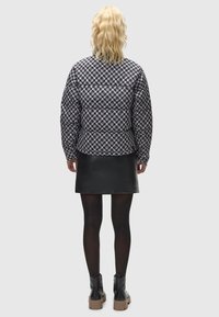 Puhasta jakna s crno-bijelim geometrijskim uzorkom, uparen sa crnom kožnom suknjom. Model nosi crne tajice i debele crne čizme.
