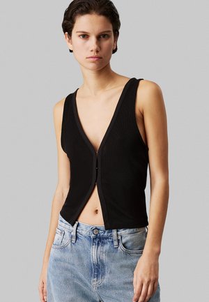 Top senza maniche nero con scollatura a V profonda e chiusura a bottoni, realizzato in tessuto a coste. Abbinato a jeans in denim blu a vita alta.