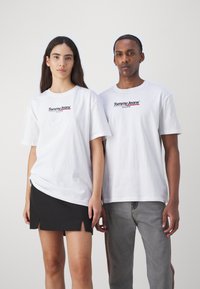 Camisetas blancas de manga corta con el logo "Tommy Jeans" en rojo y azul; combinadas con una falda negra y unos jeans grises, destacando un diseño casual.
