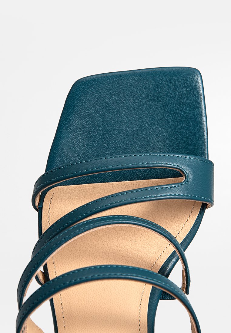 Sandale en cuir bleu canard avec un bout carré et plusieurs brides courbées. La semelle intérieure beige a une surface texturée. Fini lisse, design minimaliste.