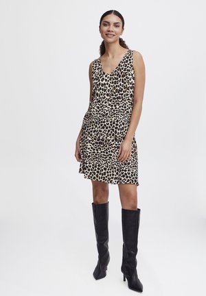 Ärmelloses Kleid mit Leopardenmuster, V-Ausschnitt, fließendem Stoff und gerafftem Saum, kombiniert mit hohen schwarzen Stilettos.