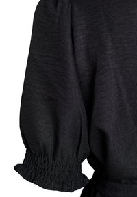 Sort stofærme med indsamlet elastisk manchet og let oppustet design mod en hvid baggrund.