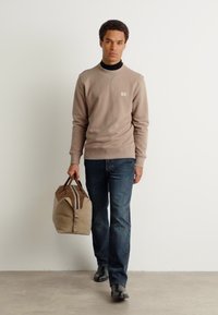 Beige sweater med struktureret stof, mørke jeans og sorte sko. Bærer en brun og beige duffelbag med håndtag og stribede detaljer.