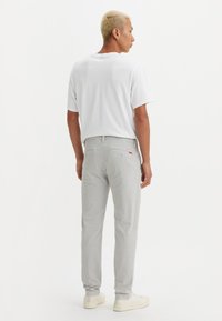 Light gray trousers made of cotton, with a straight leg design. The back features two pockets and a small label. Worn with a white shirt.
