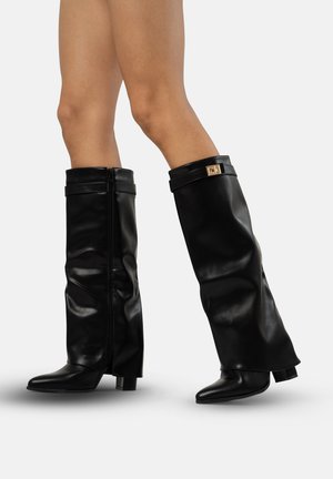 Botas de cuero negras hasta la rodilla con punta afilada, tacón cuadrado, cremallera y una correa decorativa con un acento dorado.