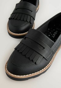 Mocassins noirs avec un dessus synthétique texturé, une frange décorative et une semelle contrastée avec un détail de couture.