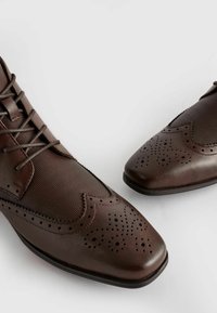Hnědé kožené boty s texturovaným povrchem, šněrovacím designem, detaily ve stylu wingtip a perforovanými akcenty na špičce a bocích.