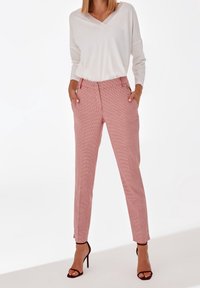 Haut blanc à col en V associé à un pantalon à carreaux rouge et blanc. Le pantalon possède des poches latérales et des jambes fuselées. Sandales à talons hauts marron.