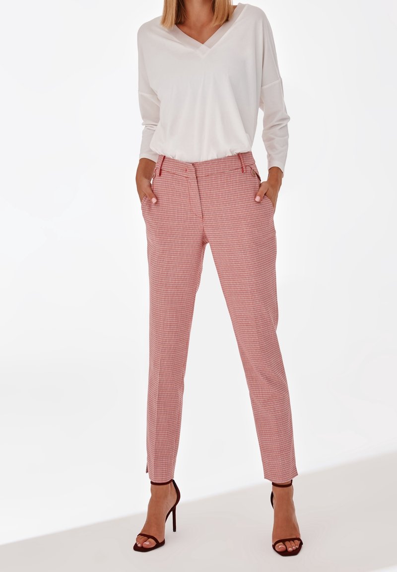 Haut blanc à col en V associé à un pantalon à carreaux rouge et blanc. Le pantalon possède des poches latérales et des jambes fuselées. Sandales à talons hauts marron.