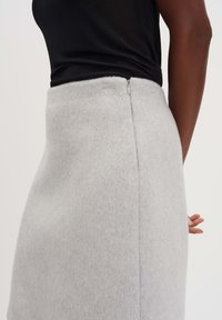 Grijze wollen rok met een zachte textuur, een getailleerd ontwerp en een discreet ritsje aan de achterkant. Gestyld met een zwarte top.