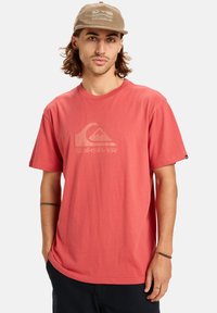 Tričko s krátkým rukávem v korálové barvě se světlejším logem Quiksilver. Měkký bavlněný materiál, volný střih, jednoduchý design, žádné vzory ani akcenty.