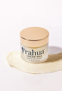 Pot de cire crème Rahua avec couvercle doré sur surface blanche, cire crème étalée en tache texturée sous le contenant.