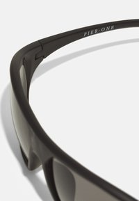 Schwarze Sonnenbrille mit einem schlanken Design, ausgestattet mit dunklen Gläsern und einem gebogenen Rahmen. Der Markenname "PIER•ONE" ist am Bügel sichtbar.