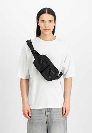 Sacola de ombro preta com dois bolsos frontais com zíper e alça ajustável, feita de material resistente. Design simples e forma compacta.