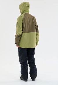 Grøn og brun vandtæt jakke med hætte. Har et farveblok design, tekstureret stof og justerbare manchetter. Bagansigt vist.