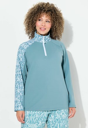 Vaaleansininen pitkähihainen sweatshirt korkean kauluksen kanssa, jossa on valkoinen vetoketju ja teepaidan hihassa teal- ja valkoisia abstrakteja kuvioita.