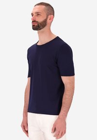 T-shirt blu navy a maniche corte in un tessuto morbido con colletto rotondo, vestibilità rilassata e design pulito. Indossato con pantaloni bianchi per un contrasto.