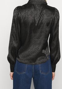 Musta satiinipusero, jossa on ilmavat pitkät hihat, kaulus ja hienovarainen kukkakuvio. Yhdistetty sinisiin farkkuihin, joissa on taskudetalji.