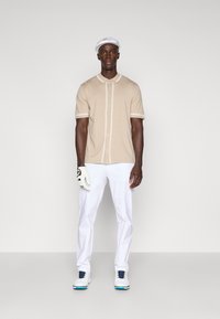 Šviesiai ruda trumpomis rankovėmis polo marškiniai su baltais kraštais, užtrauktuku. Balti kelnės, golfui skirtos avalynės su juodais akcentais ir balta kepure. Juoda pirštinė kairėje rankoje.