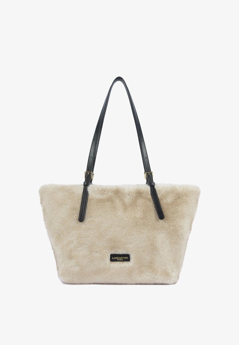 Sac cabas en fourrure douce beige avec des sangles réglables en cuir noir et une petite étiquette noire indiquant Lancaster Paris.