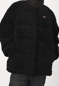 Czarna polarowa kurtka z zamkiem błyskawicznym, z teksturowanej tkaniny, wyściełanym fasonem i małym logo na klatce piersiowej.