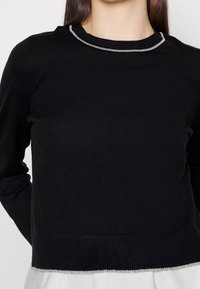Czarny sweter z długimi rękawami, ozdobiony teksturowaną srebrną lamówką przy dekolcie i dole, wykonany z miękkiej dzianiny.