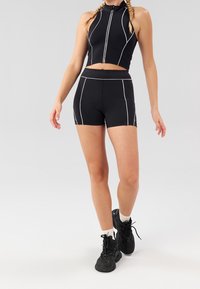 Černý sportovní crop top s vysokým límcem a bílým lemováním, doplněný černými kraťasy s vysokým pasem a bílými detaily. Kombinováno s černými teniskami.