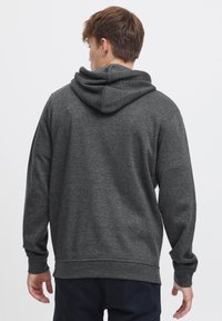Sudadera gris con una tela suave y texturada. Presenta una gran capucha, mangas largas y un corte relajado. Variación sutil de color en toda la prenda.