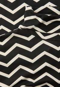 Czarna tkanina z białym wzorem w zygzaki, z naprzemiennymi kształtami chevron. Miękka tekstura z widocznymi zagnieceniami.