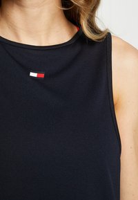 Černá sportovní tílko bez rukávů s malým červeným, bílým a modrým logem na hrudi. Texturovaná látka s kulatým výstřihem.