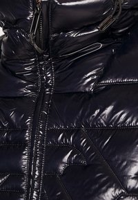 Nafukovací bunda z lesklého námořnického materiálu, s vysokým límcem, zipovým zapínáním a prošívaným vzorem s diagonálními akcenty.