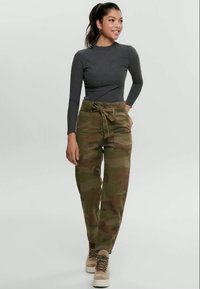 Camo cargo pants in earthy tones with a tied waist, paired with a fitted gray long-sleeve top and beige lace-up boots. Smooth texture.