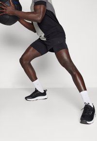 Svart och grå atletisk outfit med en åtsittande design, kombinerad med svarta träningsskor och vita strumpor, hållandes en viktad medicinboll.