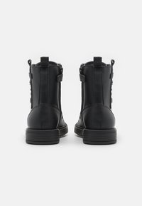 Botas de cuero negras hasta el tobillo con textura suave, cierre de cremallera y suela de goma resistente. Vista trasera con detalle de tira de agarre.