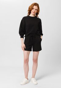 Černá mikina a šortky z měkké látky, s elastickým pasem a stahovací šňůrkou, doplněné o bílé tenisky. Jednoduchý design.
