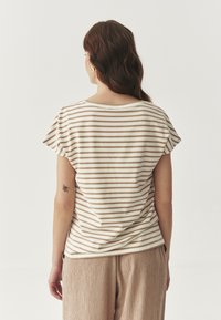 Polo bej cu dungi, cu mâneci scurte și evazate, și guler rotund, asortat cu pantaloni largi dintr-un material texturat, de culoare maro deschis.