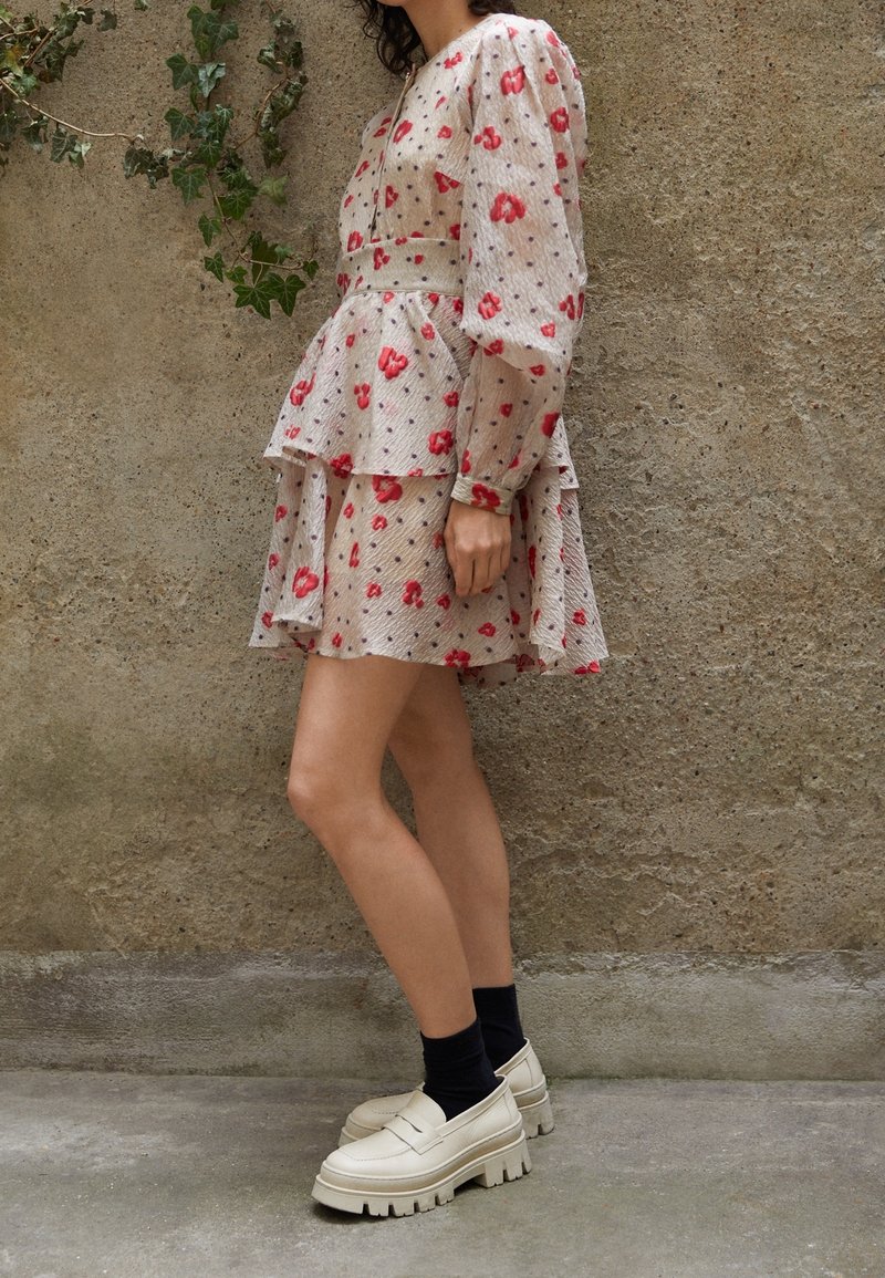 Robe à motif floral en tissu transparent et texturé ; dotée de manches bouffantes, d'un ourlet peplum et d'une palette de couleurs beige. Chaussures compensées blanches épaisses.
