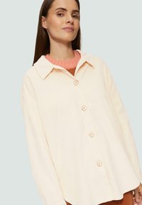 Crème corduroy overhemdjasje met een puntige kraag, zes knopen en een ontspannen pasvorm. Gelaagd over een roze geribd sweatshirt.