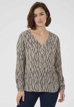 Blouse à col en V en tissu léger et transparent, avec un motif ondulé beige et noir. Manches longues avec des fronces légères aux poignets.