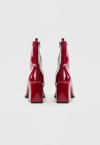 Bottines en cuir verni rouge avec un talon bloc, fermeture éclair à l'arrière et une finition lisse et brillante.