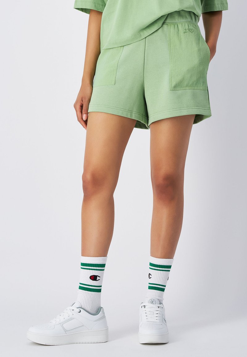 Bermuda verdi in cotone con una vestibilità comoda, dotate di tasche laterali. Abbinati a sneakers bianche e calze bianche con righe verdi.