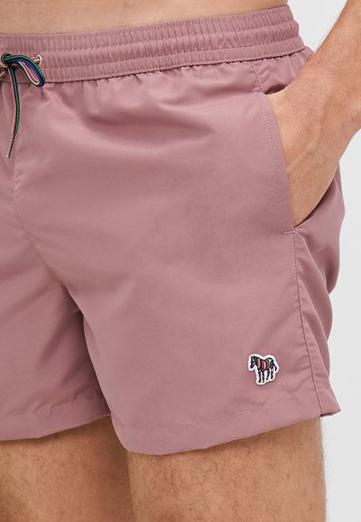 Shorts de bain roses clairs en tissu lisse avec une taille élastique, portant un logo zèbre brodé multicolore sur le côté gauche.