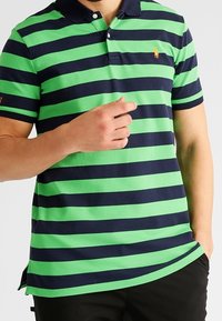 Grön och marinrandig polo skjorta med krage, tre knappar och liten broderad logotyp på bröstet. Korta ärmar och slim fit.