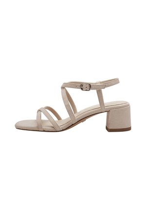 Beige suede sandal with a block heel, featuring crisscross straps and an adjustable ankle buckle for a secure fit. Smooth texture.
