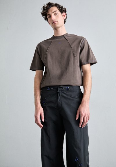 Brown short-sleeve t-shirt with a ribbed neckline, paired with loose-fitting black pants featuring blue accents and drawstrings.