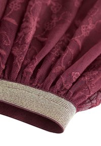 Tessuto di pizzo bordeaux con una consistenza arricciata e un elastico a strisce dorate metalliche all'orlo. Dettaglio morbido e intricato del motivo floreale.