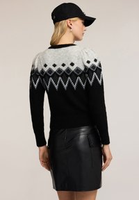 Maglione a maglia nero e grigio con motivi a diamante, caratterizzato da maniche a sbuffo e una finitura strutturata. Abbinato a una gonna di pelle nera.