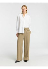 Bílá košile s dlouhými rukávy, sloučena s volnými, béžovými, texturovanými kalhotami. Černé špičaté baleríny doplňují celý outfit.