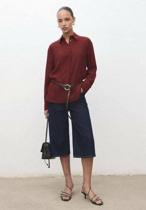 Camisa burdeos de botones, pantalones de mezclilla anchos oscuros, cinturón marrón con hebilla circular, bolso negro y sandalias de tacón negro con tiras.